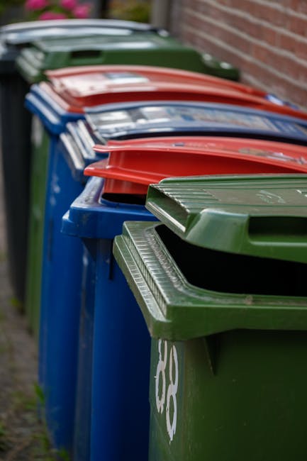 A large outdoor scene displaying a variety of waste materials and discarded items arranged for collection, including multiple stacks of empty fruit and vegetable crate boxes with colorful printed labe